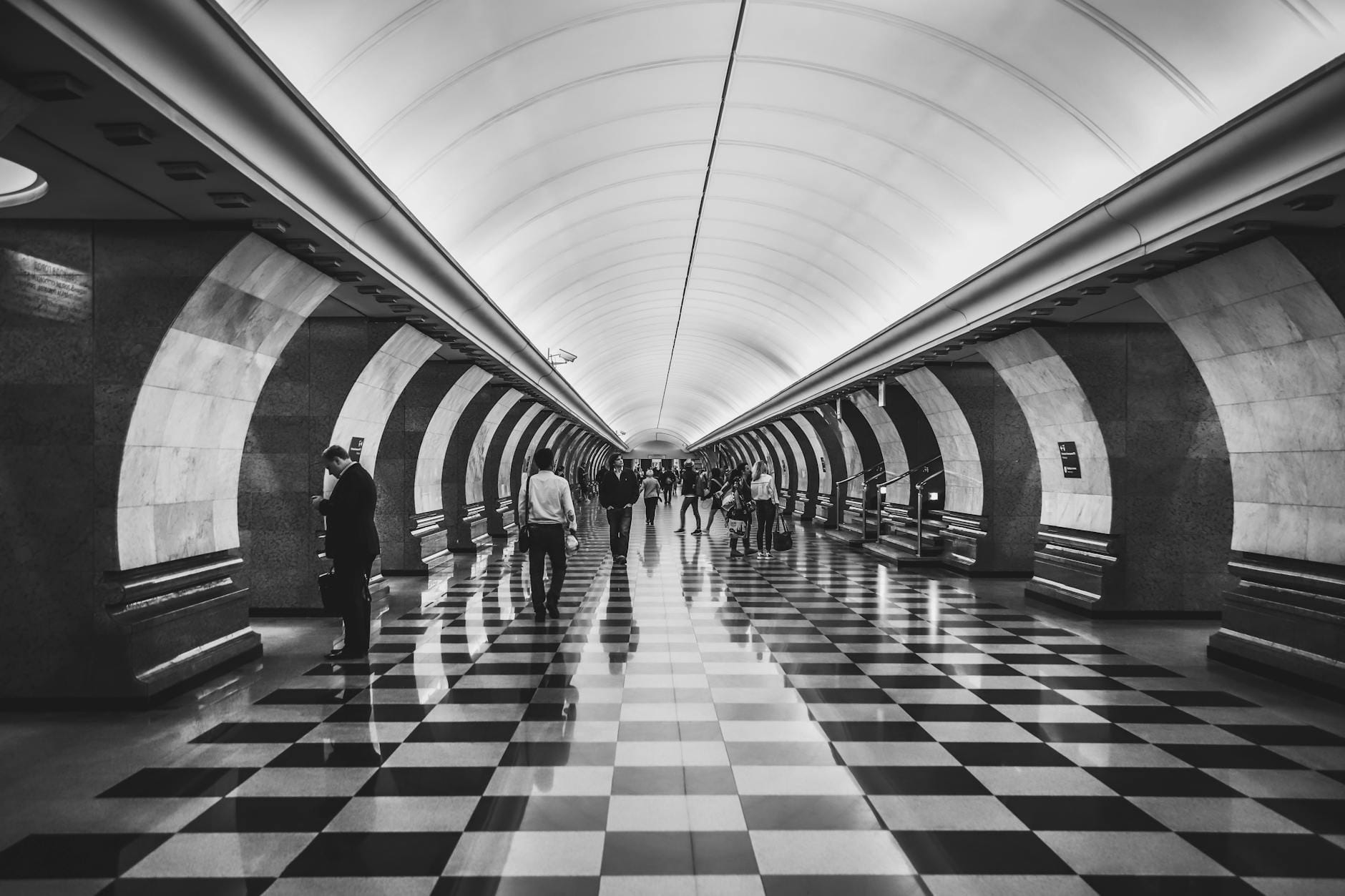 Black and white image of people walking in a Moscow subway station with distinctive architecture.
